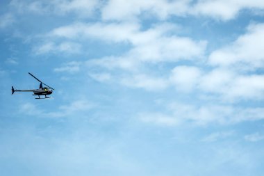 Açık mavi gökyüzü arka planda helikopter silueti.