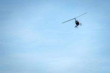 Açık mavi gökyüzü arka planda helikopter silueti.