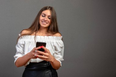 Şaşkın sürpriz kız açık ağız ile telefon bakarak, gri boş stüdyo arka plan üzerinde izole cep telefonu tutan sosyal medya mobil online içerik şok genç kadın müşteri şaşırttı