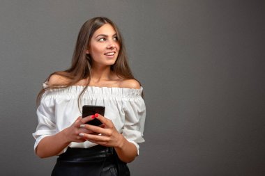 Cep telefonu uygulamaları kullanarak gülümseyen genç kadın, mobil cihaz ekranına bakan çekici kadın, sosyal ağda online sohbet kız, iyi haber okuma, mesaj, stüdyo arka planda izole