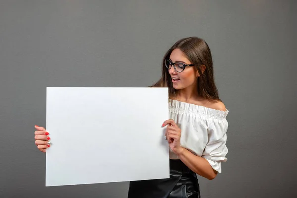 Красива жінка тримає порожній рекламний щит ізольовано на сірому фоні — стокове фото