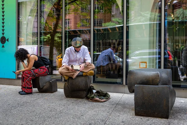 New York, USA - 6 giugno 2019: Sul marciapiede, un uomo si siede su una panchina e legge un libro . — Foto Stock