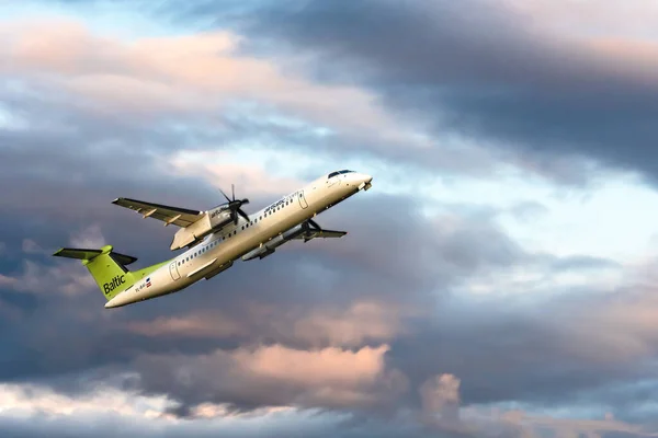 Samolot pasażerski Yl-Bai - Bombardier Dhc-8-400 odlatuje z lotniska Rix o zachodzie słońca. Jako Air Baltic Corporation, jest przewoźnikiem bandery Łotwy — Zdjęcie stockowe
