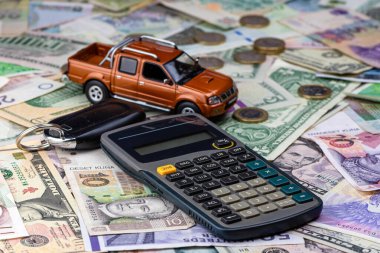 Çeşitli ulusal para birimi banknotlarında hesap makinesi, anahtarlar ve oyuncak araba. Satın alma, kiralama ve araba bakımı maliyeti