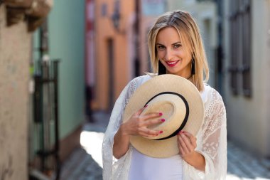 Güneş şapkalı, açık renk elbiseli güzel sarışın kadın portresi. Sokakta poz veren modacı kız.