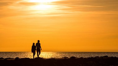 Gün batımının altın saatinde iskelede yürüyen ve bisiklete binen insanların silueti