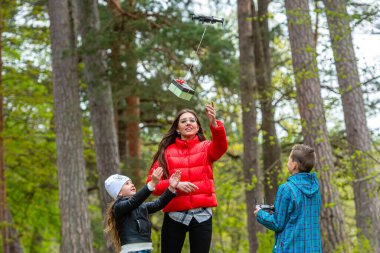 Parkta iki kız kardeş ve bir erkek kardeş sıcak bir bahar gününün tadını çıkarın ve bir dronla eğlenin, yaşam tarzı ve eğlence kavramı.