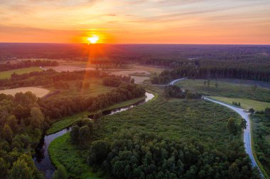 Günbatımında kıvrımlı bir nehri, ormanları ve kır yolları olan Letonya kırsal manzarası, hava manzarası