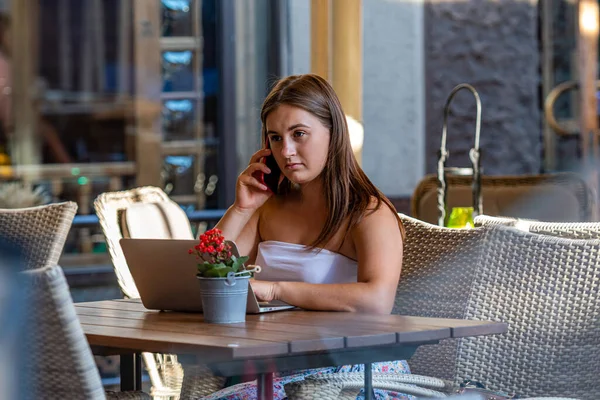 young woman work on laptop and using phone sitting in street cafe, remote learning and work concept