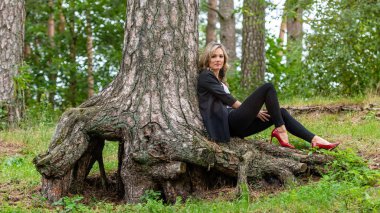 Zarif sarışın bayan ağaçların orada oturuyor ve sessizliğin tadını çıkarıyor.