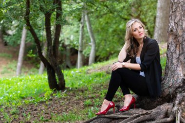 Zarif sarışın bayan ağaçların orada oturuyor ve sessizliğin tadını çıkarıyor.