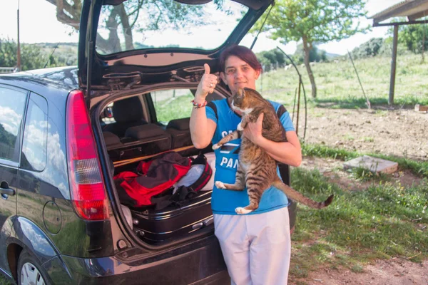 girl ready to go with the bags loaded in the car with her cat in hand