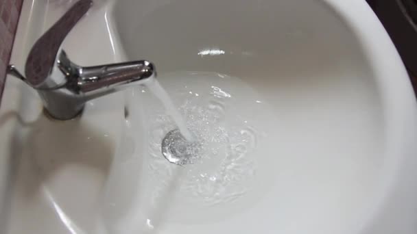 Water flowing from the faucet of the bathroom sink and down into the drain, seen in slow motion — Stock Video