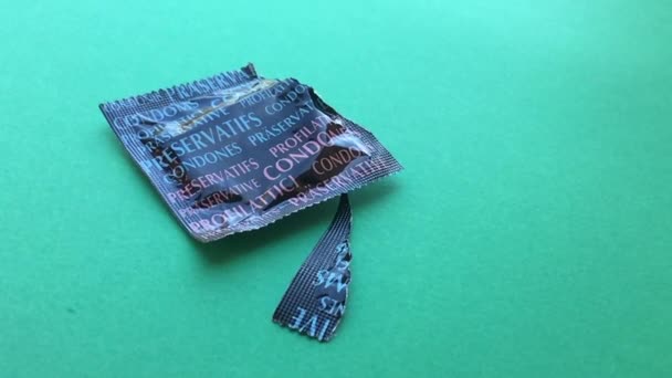 Geschlossenes Kondom, das fällt und auf dem grünen Hintergrund hüpft, Frauenhände öffnen Kondom auf grünem Hintergrund, gesehen in Zeitlupe — Stockvideo
