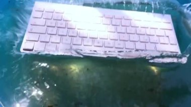 beyaz kablosuz bilgisayar klavyesi yavaş çekimde su püskürtme görünümü içine düşüyor