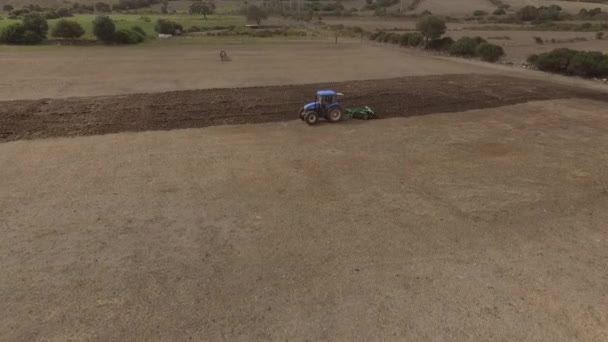 Беспилотный летательный аппарат голубого трактора с плугом в эксплуатации в полевых условиях — стоковое видео