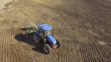 Mavi traktörün hareket halindeki hava görüntüsü tohum ektikten sonra toprağı eziyor