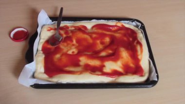 Damlaya damlaya damlaya dökülen domates sosu ekşi hamurdan yapılmış kare bir tavaya bulaşır.