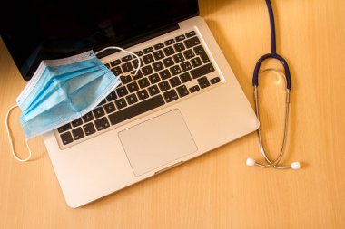 Bilgisayar klavyesinde duran stetoskop, eldiven ve maske gibi tıbbi araçlar dizüstü bilgisayarların ve doktorların bilgisayar ve tıbbi malzemelerle onarımının bir sembolüdür.