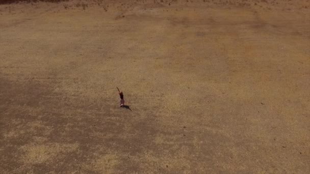 Visão aérea da menina feliz que se vira sozinha em um campo árido com as mãos no céu como um símbolo de liberdade — Vídeo de Stock