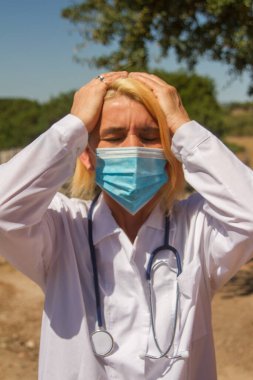 Sarışın kadın doktor göz ve kulak cerrahisi maskesi takıyor. Virüs hakkında olumsuz şeyler duymak ya da görmek istememenin sembolü olarak.