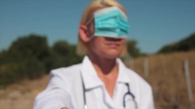 Sağlık maskesi takan genç sarışın kadın doktor ve gözleri kulaklarında ya da kafalarında hayır diyen kamera önünde el parmağı olan kadın doktor.