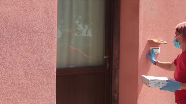 Female pizza delivery man delivering two cartons of Italian pizza directly to the front door with health mask over his mouth and everyone looks happy making the ok gesture — Stock Video