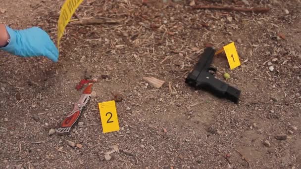 Сині рукавички детектива, що фіксують жовту попереджувальну стрічку, не проходять поруч із свідченням злочину на місці злочину, як пістолет і кривавий ніж — стокове відео