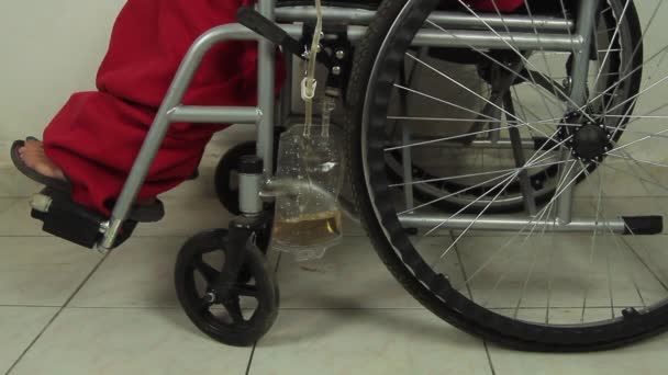 Закрыть инвалида в инвалидном кресле в больнице или клинике, к которому прикреплен дренажный пакет катетера мочи, заполненный мочой — стоковое видео