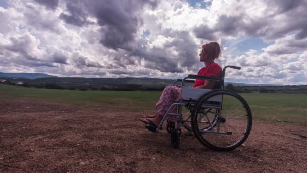 Pauză de timp a unei fete cu dizabilități care stă într-un scaun cu rotile în mijlocul unui câmp verde în mediul rural, cu un cer plin de nori de ploaie negri și albi în mișcare — Videoclip de stoc