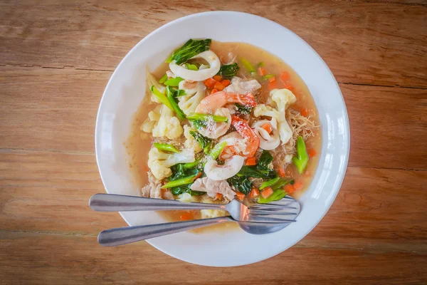 Deniz ürünleri içinde kalın et suyu ile ahşap masa üzerinde beyaz plaka üzerinde ince Pirinç Noodle yemekleri servis ile üstten görünüm