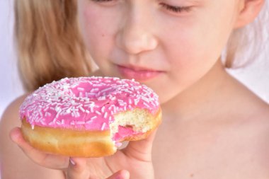 küçük kız pembe bir çörek yiyor