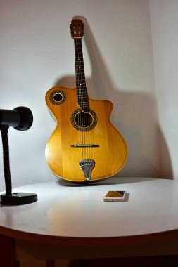 Beyaz duvarın yanındaki akustik gitar ve cep telefonunun yakın çekim görüntüsü 