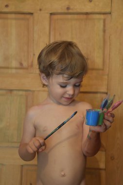 Cute little boy playing with paints and brush
