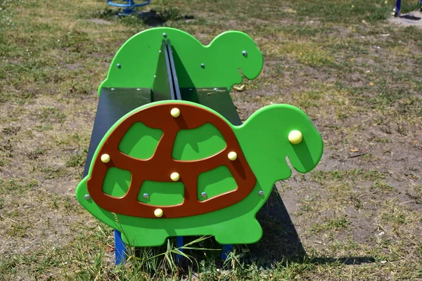 wooden green turtle swing in playground field, outdoors