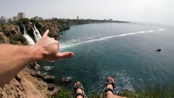 Legs of Man Sitting on the Cliff and Enjoy View of the Picturesque Lower Duden Waterfall Falling into the Sea in Antalya, Tyrkia. POV . – stockvideo