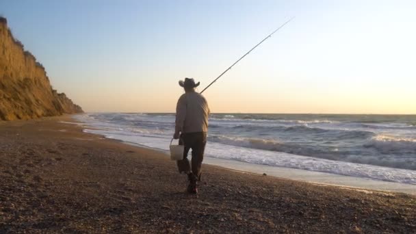 Äldste fiskare i hatt fiske vid soluppgången på kusten av havet vid blåsigt väder — Stockvideo