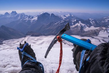 İlk kişi görüntüleyebilir vücut ve uzak manzara. Krampon buz baltalı adam bacaklarda dağın biraz dinlen. Trekking botları arka ayaklarda Kafkasya