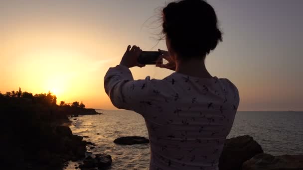 Adorabile ragazza bruna caucasica in abito leggero utilizzando Smartphone per sparare alla scogliera sopra il mare all'alba — Video Stock