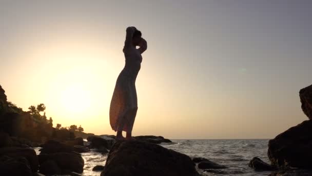 Schattig Kaukasische Brunette meisje in licht jurk dansen op de rots in de zee bij zonsopgang — Stockvideo