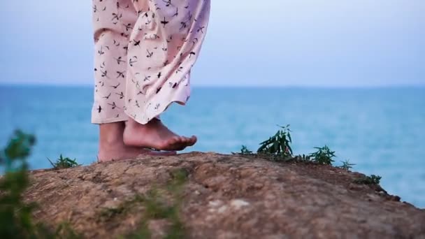 Füße eines Mädchens in hellem Kleid, das bei Sonnenaufgang am Fuße der Klippe über dem Meer spaziert — Stockvideo