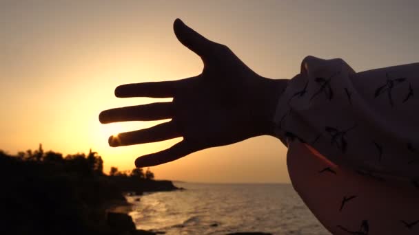 Dívka hraje s vycházejícího slunce na moři v době úsvitu. Zpracování sluneční paprsky mezi prsty. — Stock video