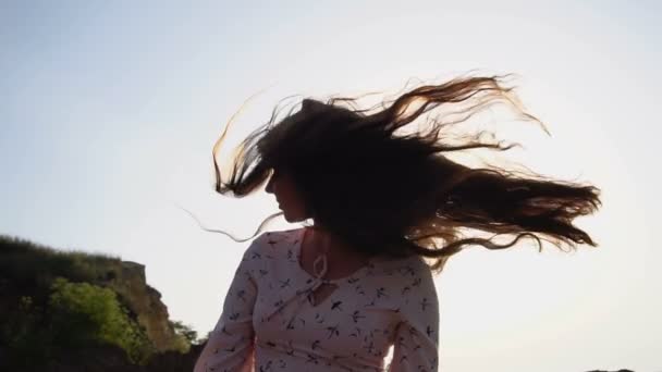 Portret van schattige Kaukasische Brunette meisje in licht roze jurk spelen met haar lange mooie haren bij zonsopgang. — Stockvideo