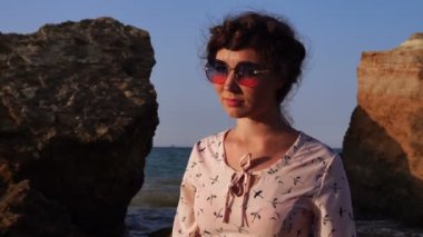 Güneş gözlüğü ve ışık pembe elbise oturmak gündoğumu zaman taş sevimli beyaz esmer kız