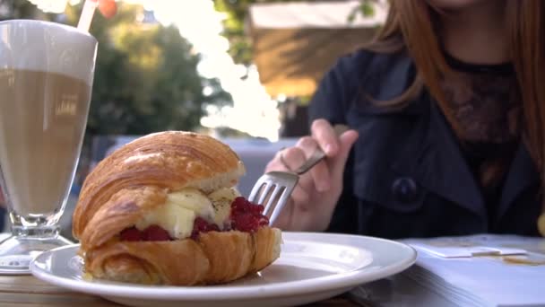 Attraktive moderne junge Frau isst Croissant und trinkt aromatischen Kaffee in einem Café auf einer Sommerterrasse. — Stockvideo