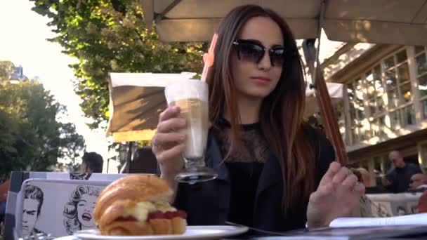 Attraktiv modern ung kvinna dricker aromatiskt kaffe på ett kafé på en sommarterrass och blad över modemagasin — Stockvideo