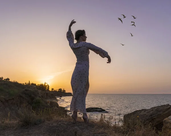Entzückende kaukasische Brünette in leichtem Kleid genießt am Meeresufer bei Sonnenaufgang. — Stockfoto