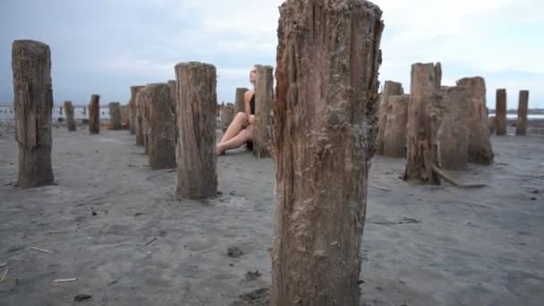 Joven rubia sentada rodeada de estacas en la costa de Salt Firth, clima nublado — Vídeos de Stock