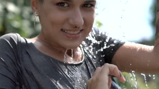 Menina bonita bonita perfurada em óculos de sol se divertindo com spray de água da mangueira no jardim. Verão Lazer e t-shirt molhada. Corpo bonito — Vídeo de Stock