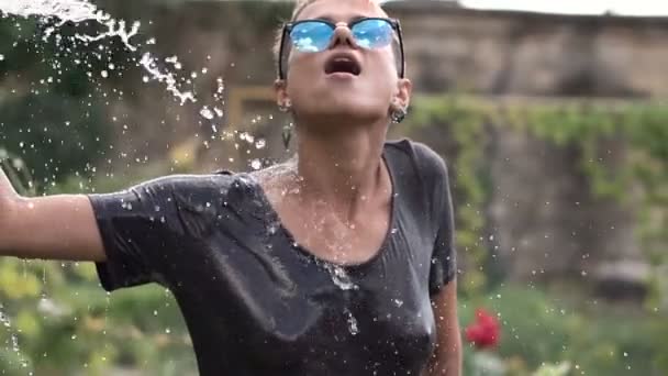 Young Pretty Pierced Girl en gafas de sol divirtiéndose con spray de agua de la manguera en el jardín. Camiseta de verano de ocio y mojada. Hermoso cuerpo — Vídeos de Stock